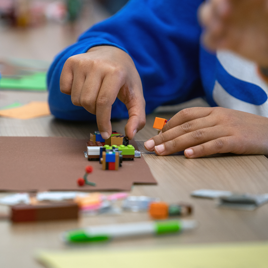 Kinderhände schieben Legoteile auf Tonpapier
