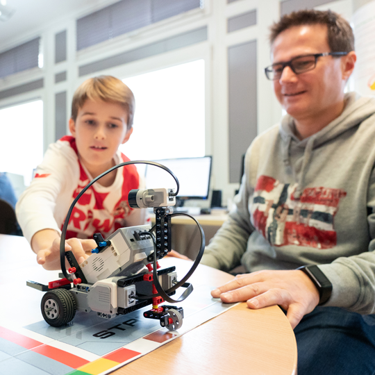 Ein Vater betrachtet zusammen mit seinem Sohn einen fahrenden Lego-Roboter