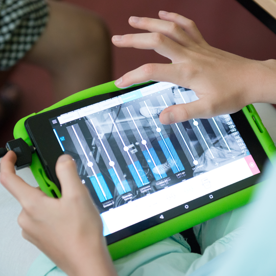 Ein Kind schiebt digitale Mischpult-Regler auf einem Tablet.