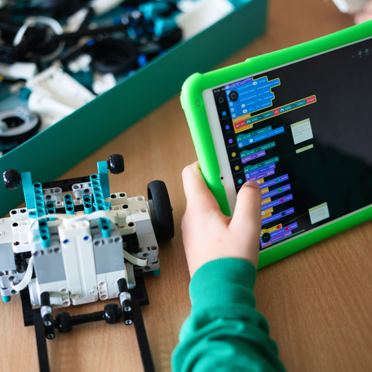 Legoteile neben einem Tablet, auf dem Programmiercode zu sehen ist