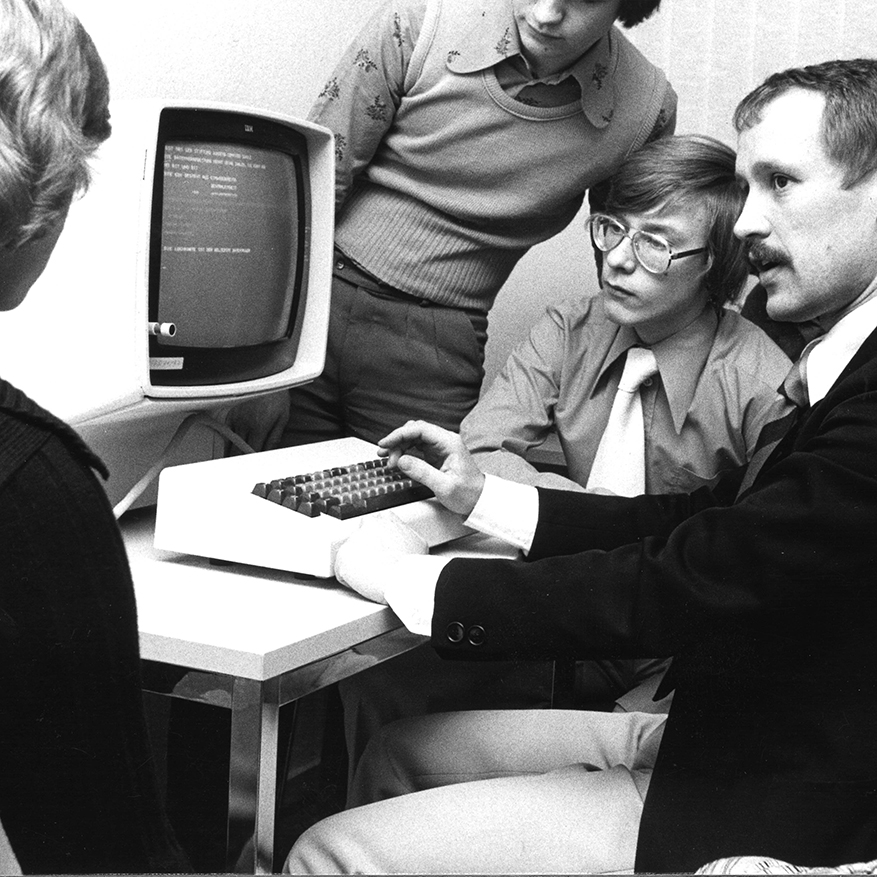 Eine Gruppe sitzt vor einem alten Computer im Jahr 1976.