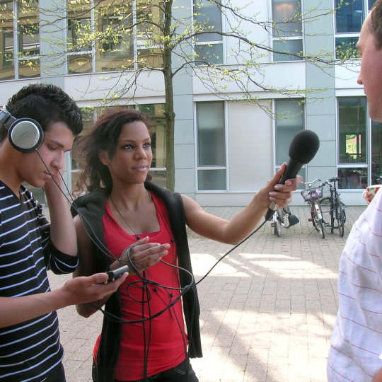 Zwei Jugendliche nehmen ein Interview mit einem Passanten auf