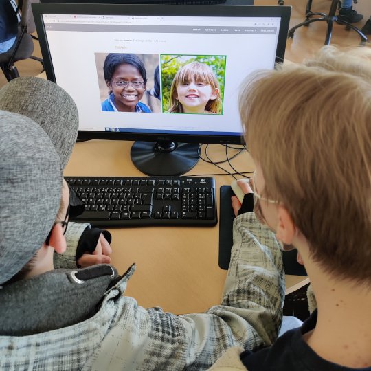 Zwei Kinder betrachten auf einem Computermonitor zwei Portraits