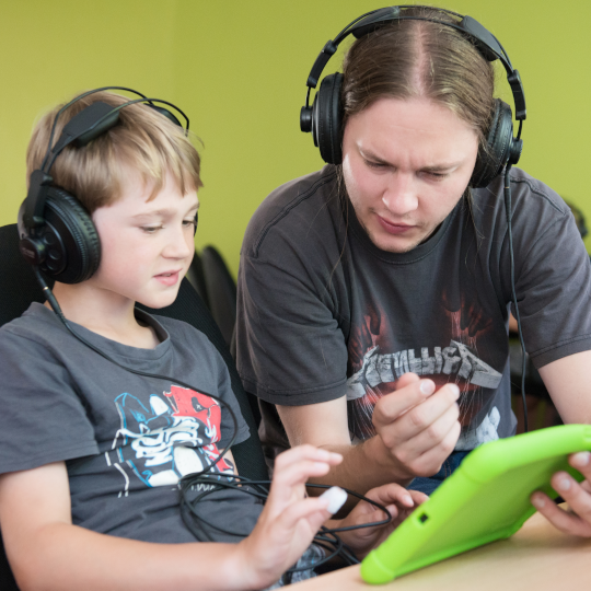 Zwei Jungen haben Kopfhörer auf und schauen auf ein Tablet