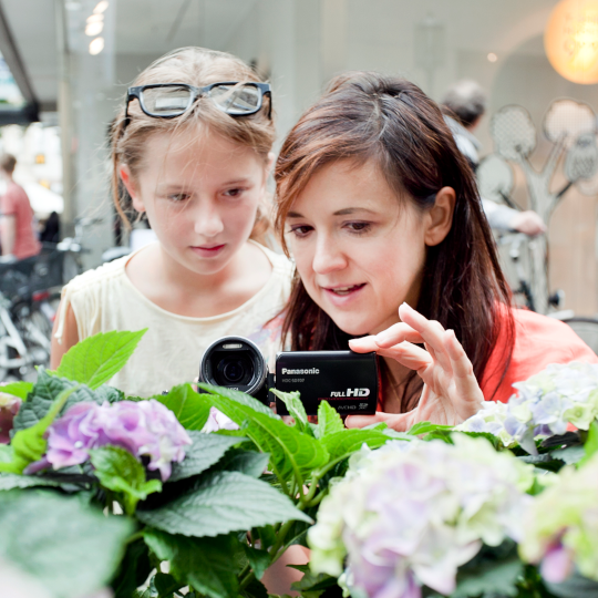 Zwei Mädchen schauen durch eine Videokamera und filmen Hortensien